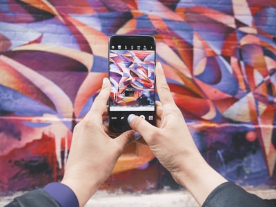白天手持 Android 智能手机并拍摄抽象墙照片的人

